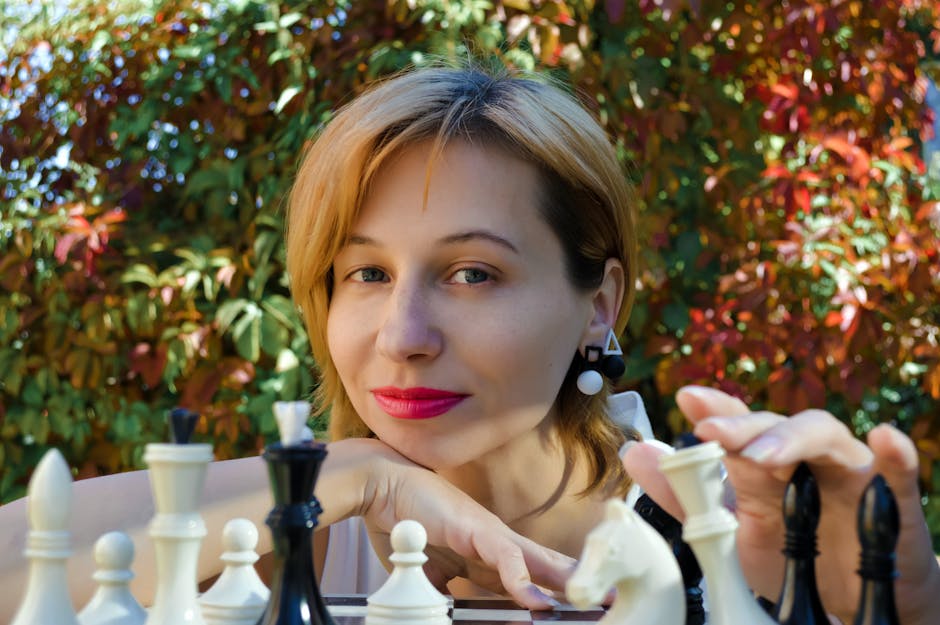 Content female player looking at camera while sitting at chess board during game on street with colorful foliage on trees