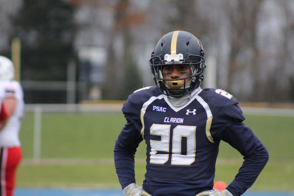 Focused American football player wearing a helmet and uniform prepared for the game on a grassy field.