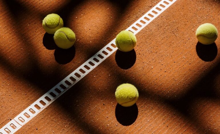 Tennis balls cast shadows on a clay court, showcasing light play and sports ambiance.