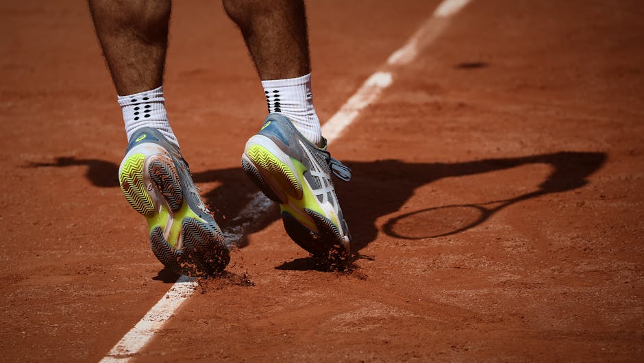 Tennis player in motion on a clay court in Paris, showcasing athletic shoes and dynamic movement.