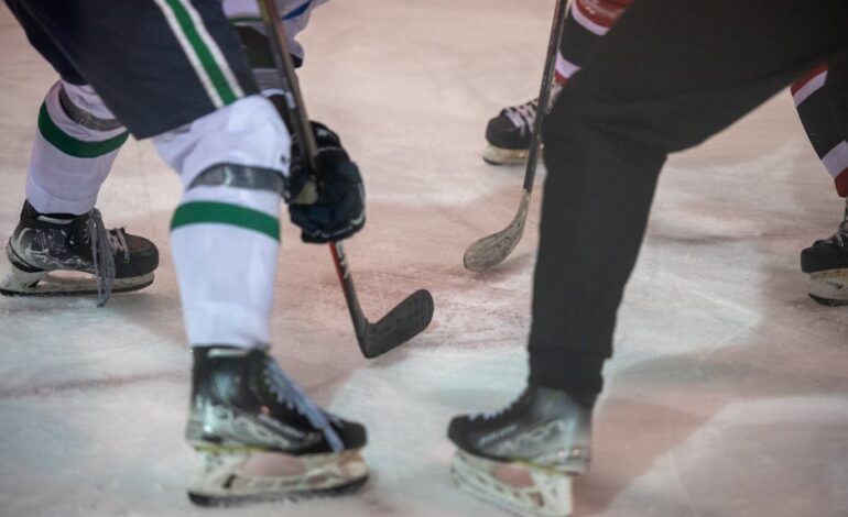 Close-up shot of ice hockey players in an intense face-off, showing skates and sticks on the ice.