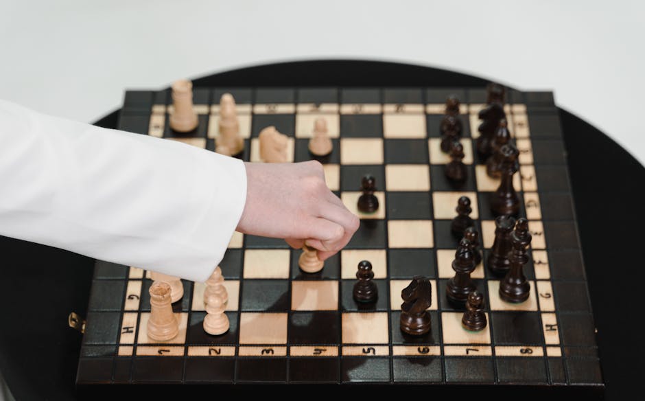Close-up of a hand strategically moving a chess piece on a wooden chessboard.