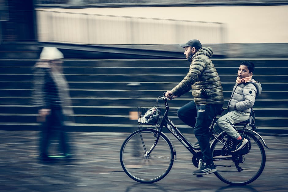 A man biking with his child on a busy street captures motion and urban life.