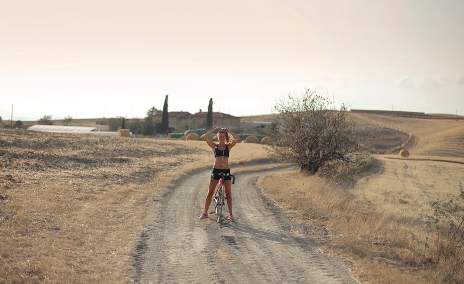 Young female in sportswear standing with cycle on road in remote countryside while doing ponytail