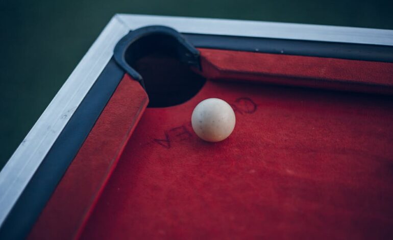 A cue ball rests near the pocket on a red-felt pool table, showing game readiness.