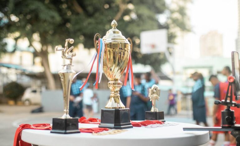 A golden trophy displayed on a table during an outdoor sports event with blurred players in the background.