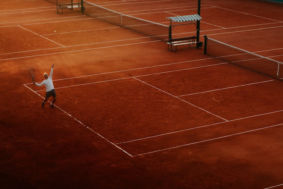 A player serves on a clay tennis court, highlighting the beauty and intensity of the sport at sunset.