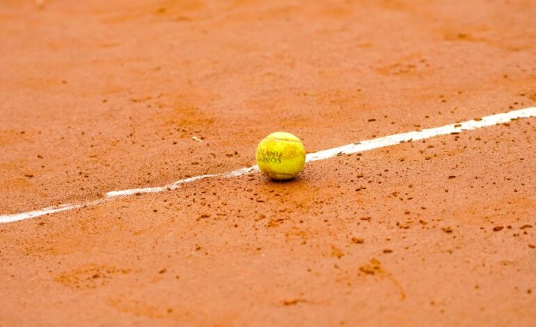 Tennis ball resting on a clay court, marked by a white line, ideal for sports themes.