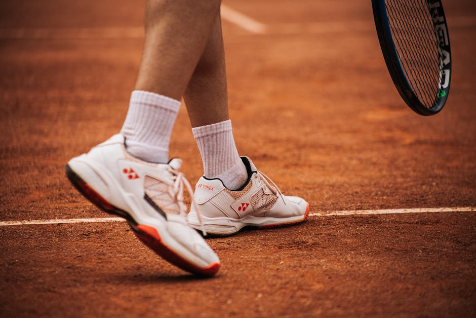 Close-up of a tennis player on a clay court preparing to serve with racket and shoes.