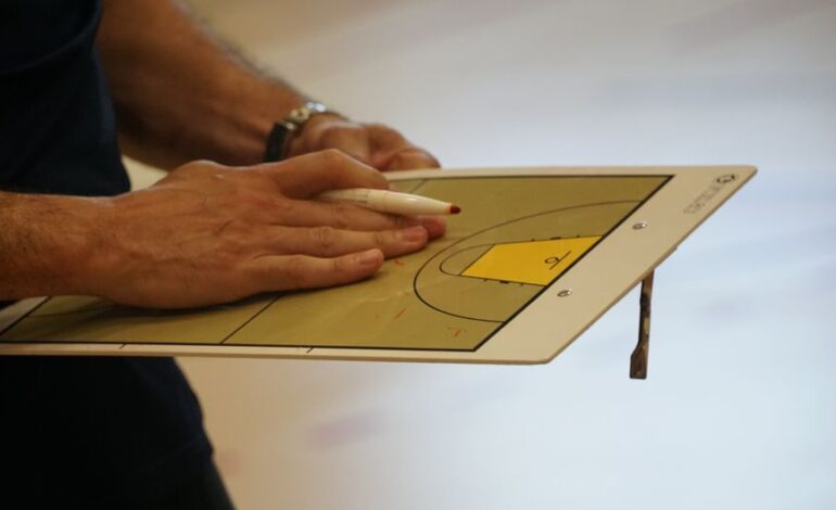 Close-up of a coach using a basketball tactics board to plan game strategy indoors.