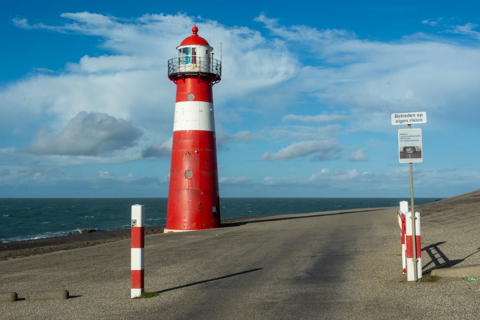 Vibrant red and white lighthouse on Westkapelle shoreline under bright sky.