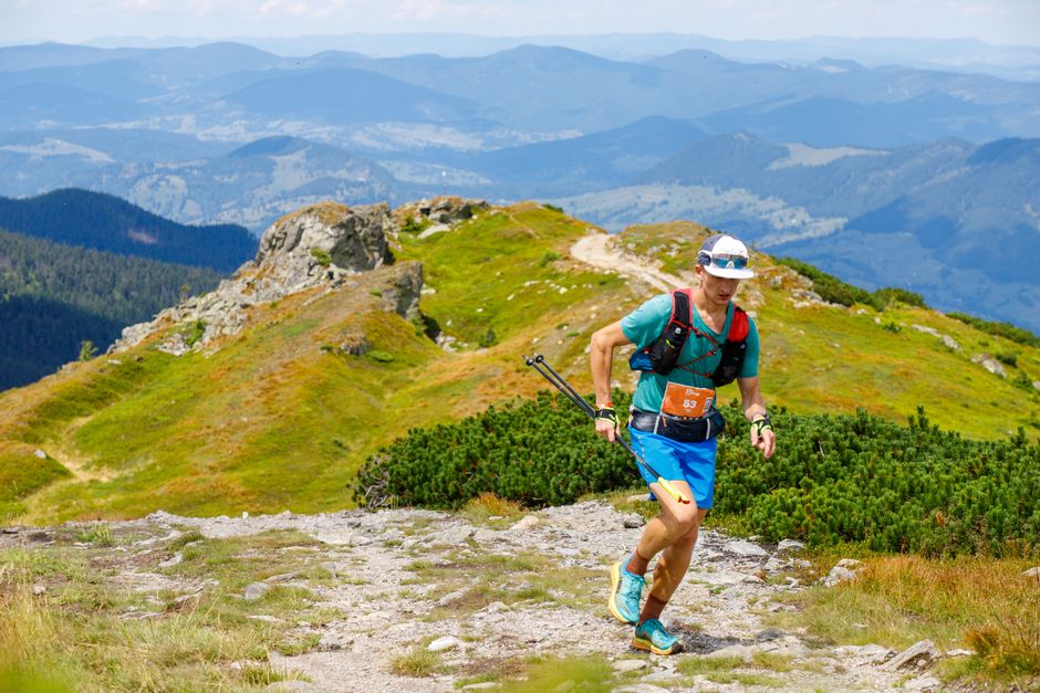 Athletic man trail running on a scenic mountain trail during the day.
