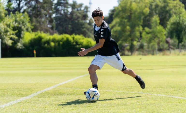 A teenager playing soccer on a sunny day, dribbling the ball on a grassy field.