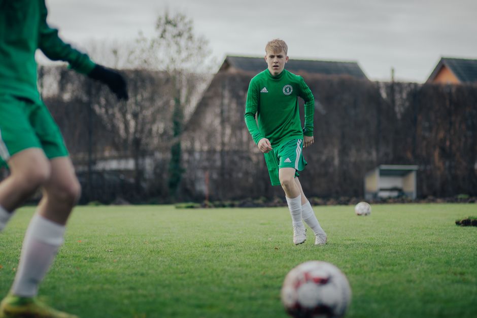 Two teenagers playing soccer on a grass pitch during daytime training session.