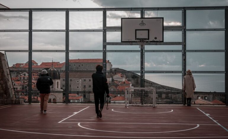 Stylish individuals on a rooftop basketball court with Dubrovnik's historic skyline in the background.
