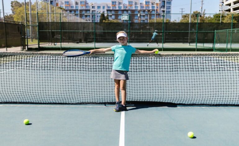 A young girl in sportswear poses with a tennis racket and ball on an outdoor court.