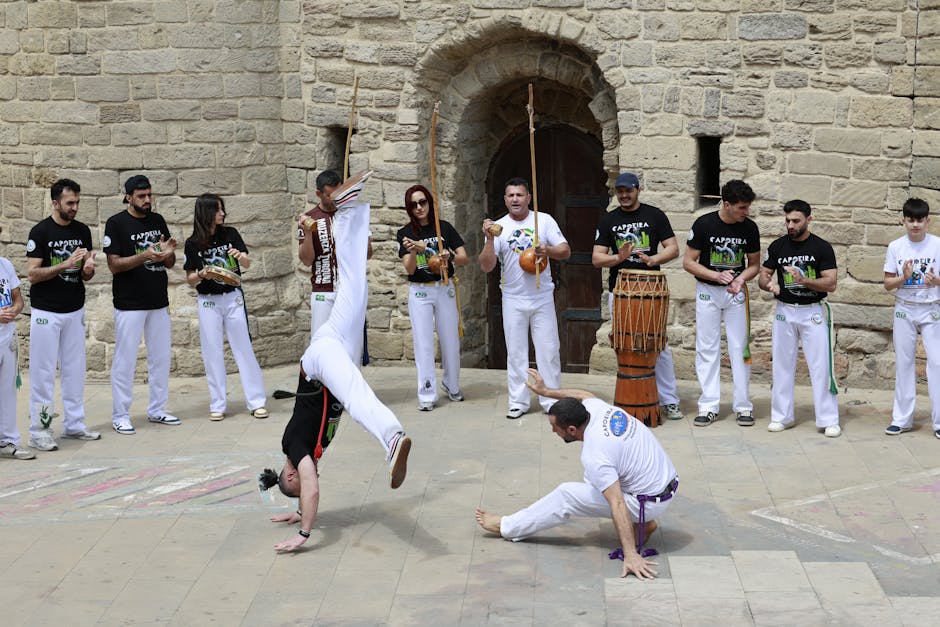 Capoeira performers demonstrating skills outdoors near historic stone architecture.