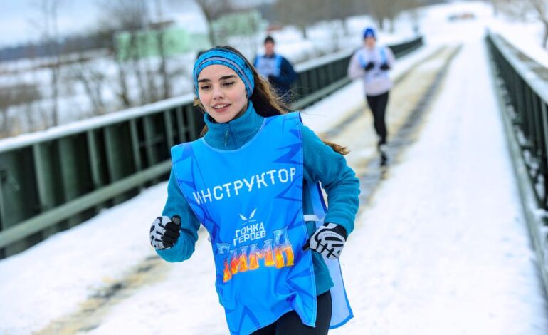 Young woman runs in winter marathon on a snowy path, wearing blue gear.