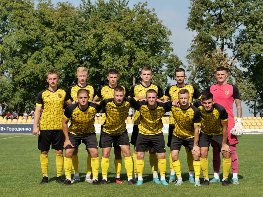 A young men's soccer team in yellow and black uniforms posing on the field before a match.