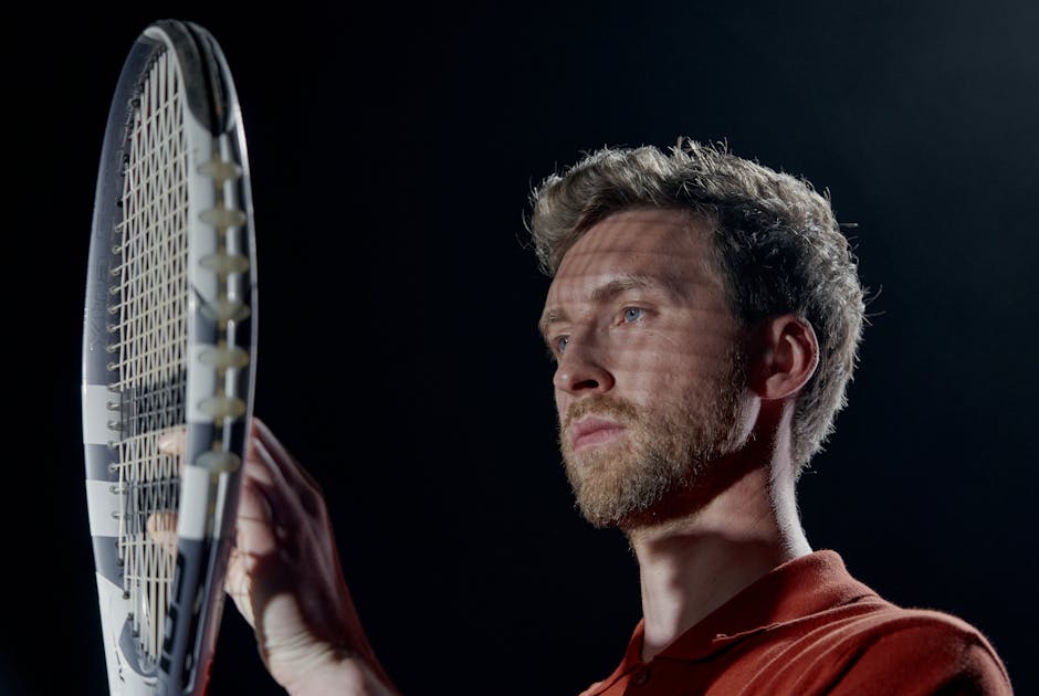 Portrait of a serious male tennis player holding a racket with a black background.