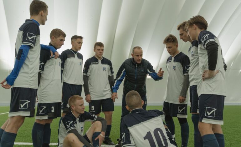 Coach giving a pep talk to a men's soccer team indoors.