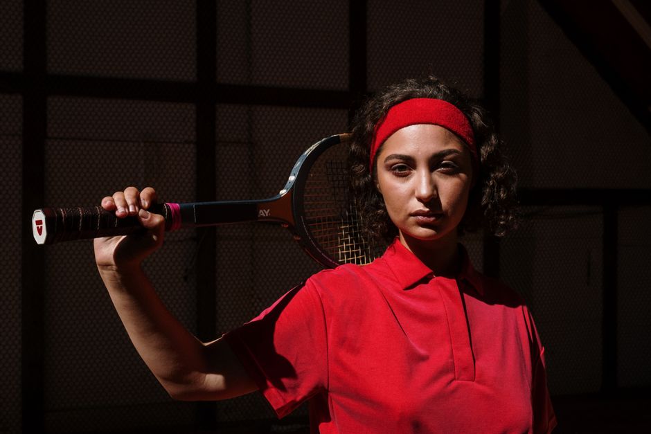 Portrait of a serious female tennis player holding a racket indoors.