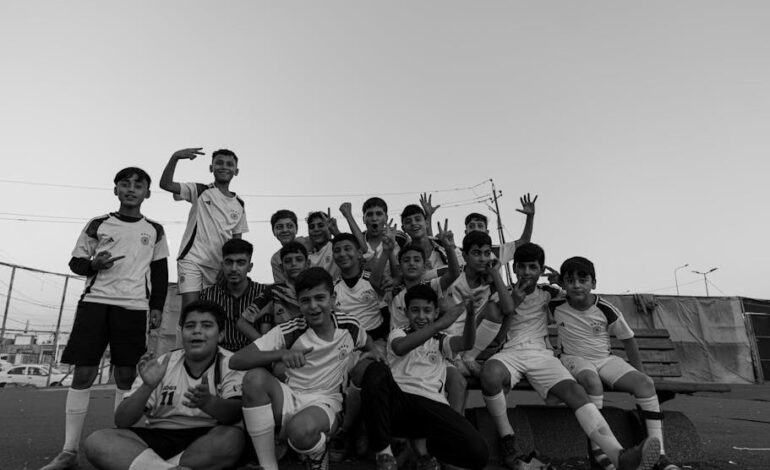Black and white photo of young boys posing cheerfully in sports uniforms outdoors.