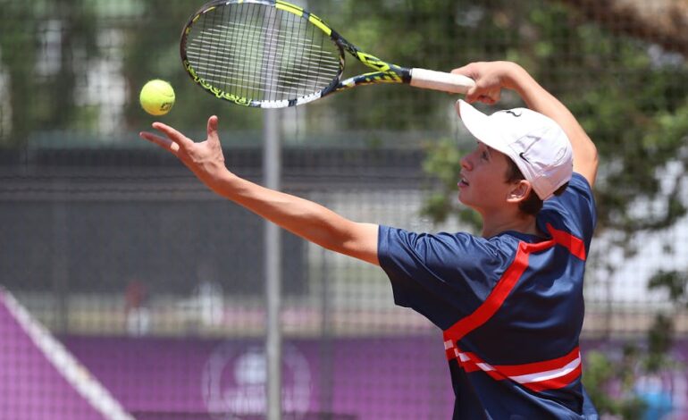 Teenage tennis player in action serving on a sunny outdoor court.