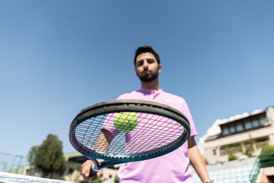 Low-angle shot of a tennis player holding a racket with a ball against a clear blue sky.