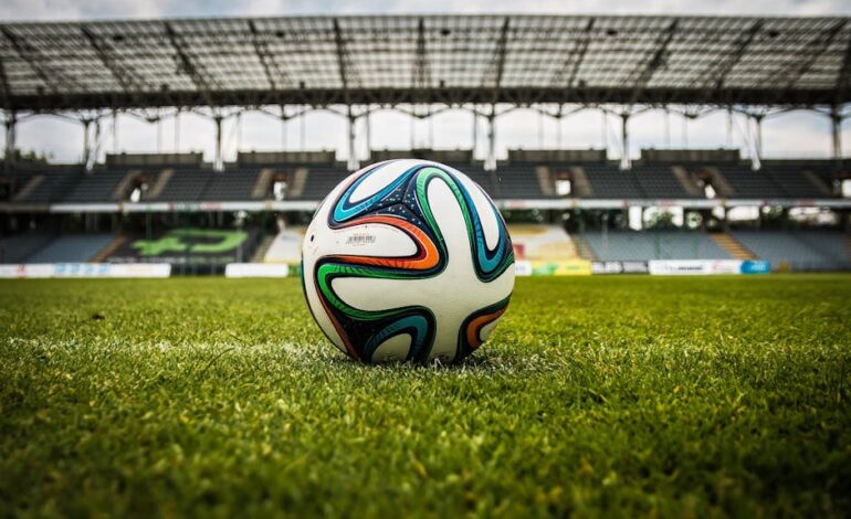 A vibrant soccer ball rests on a lush green field inside an empty stadium, capturing the essence of sports.