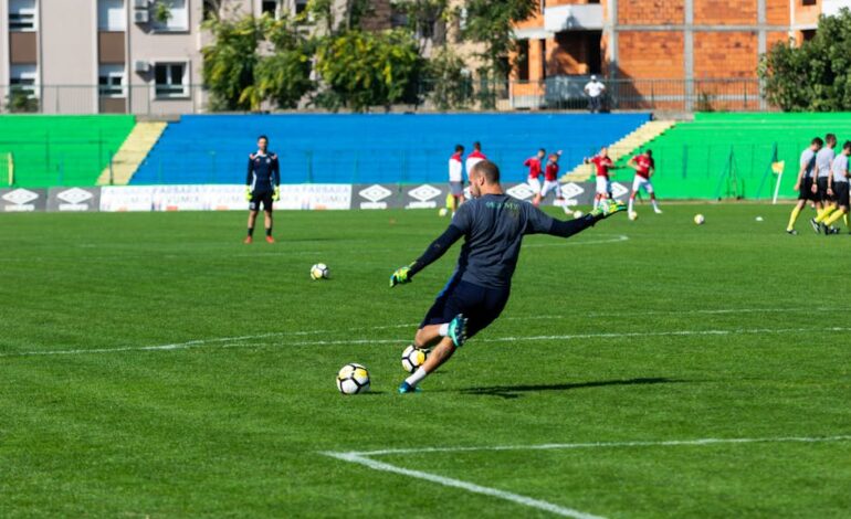 Soccer player in action during practice on a sunny day, kicking the ball on a green field.