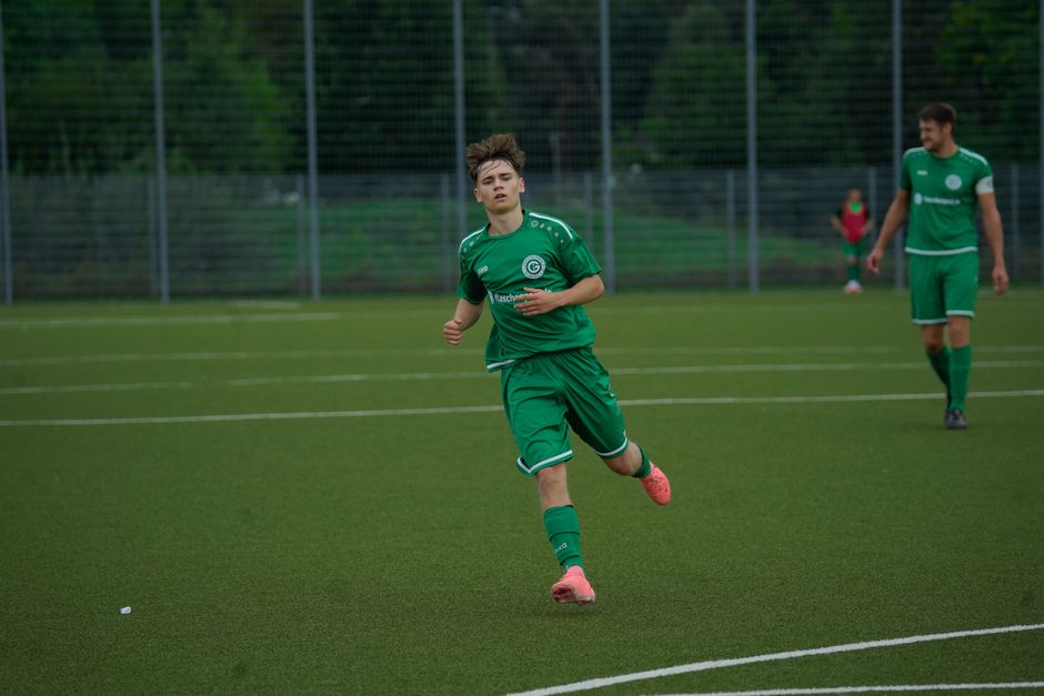 A football player in a green jersey running during an outdoor match on a grass pitch.