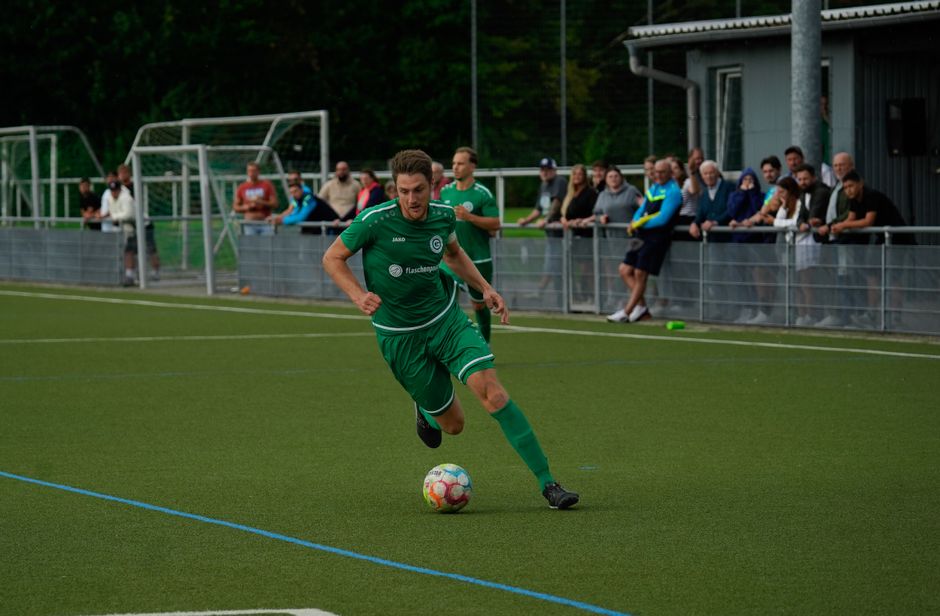 A soccer player in green dribbles the ball on a lively football pitch during a vibrant match.