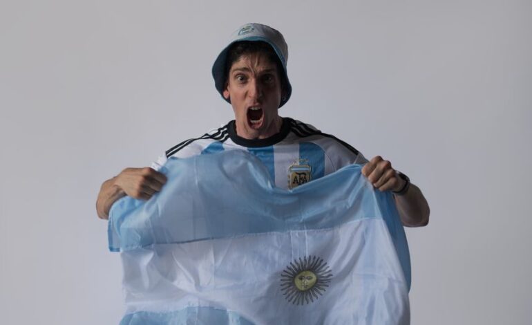 Excited Argentinian soccer fan cheering with national flag indoors.