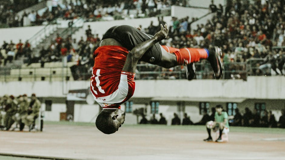 A soccer player performs a dynamic flip during a match, showcasing athletic skill and excitement.