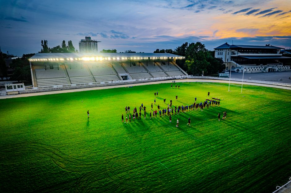 Aerial shot of a group practicing rugby under stadium lights at sunset, creating a vibrant and dynamic atmosphere.