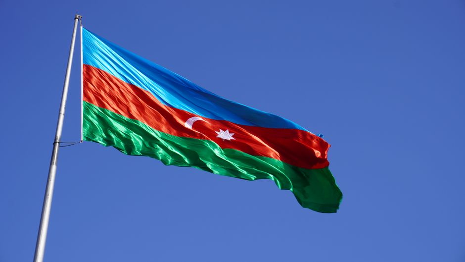 Vibrant Azerbaijani national flag waving against a clear blue sky, symbolizing national pride.