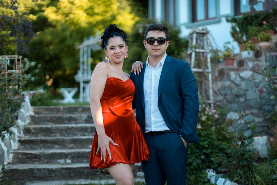 A stylish young couple poses together outdoors in formal clothing.