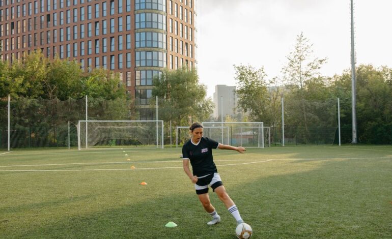 A woman practicing soccer skills on a city field with tall buildings in the background.