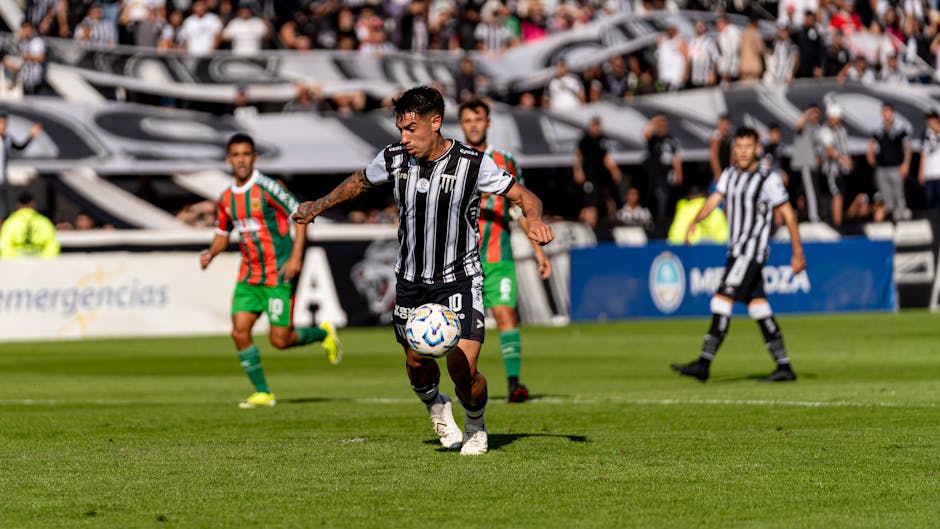 Football players in action during an intense outdoor match with a vibrant crowd in the background.