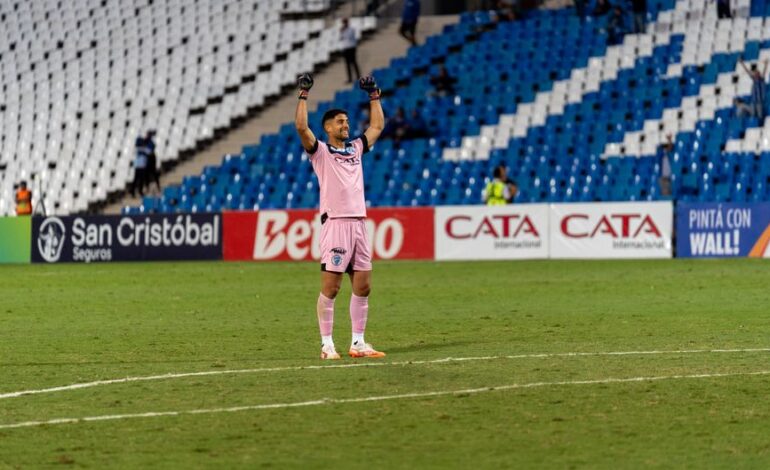 Soccer goalkeeper in pink jersey celebrating victory on the field with raised arms.