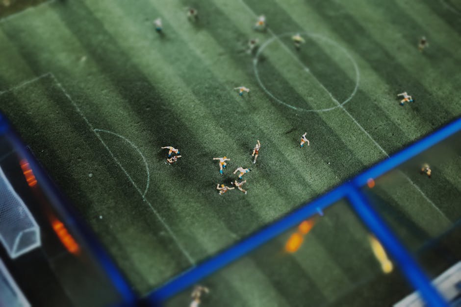 A top-down view of a miniature soccer match featuring tiny figurines on a football field.