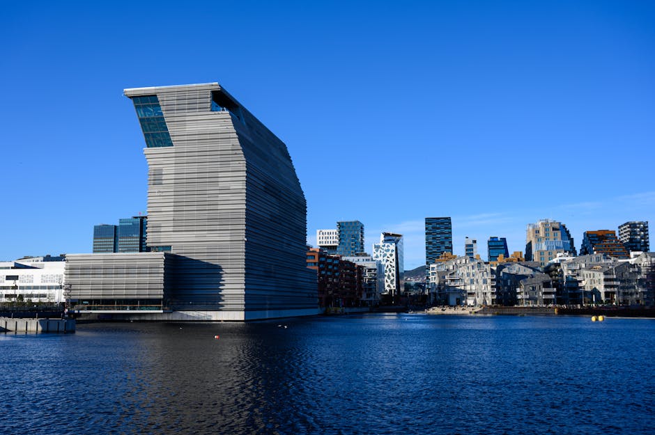 Stunning view of the contemporary Munch Museum and Oslo skyline reflected on the waterfront under a clear blue sky.
