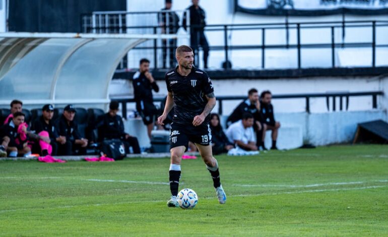 Soccer player dribbling during a match with team watching from the sidelines.