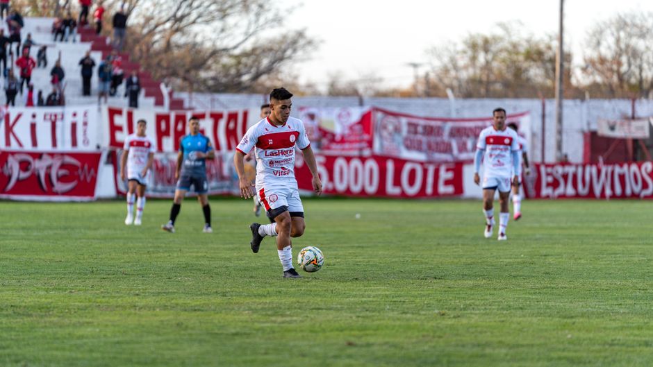 A soccer player in red and white uniform dribbles during a daytime outdoor match.