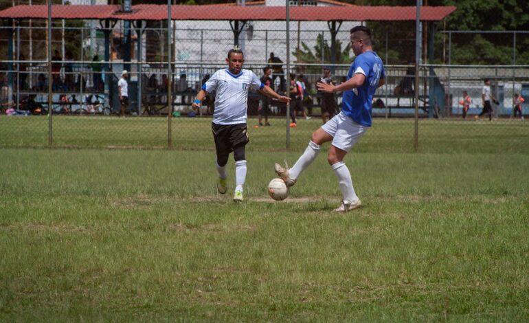 Two male soccer players competing in an outdoor match on a sunny day.