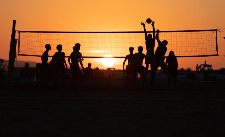 Silhouetted players enjoy a game of beach volleyball against a stunning sunset in Follonica, Italy.