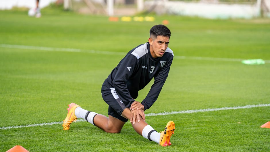 Soccer player preparing for practice by stretching in a grassy outdoor field.