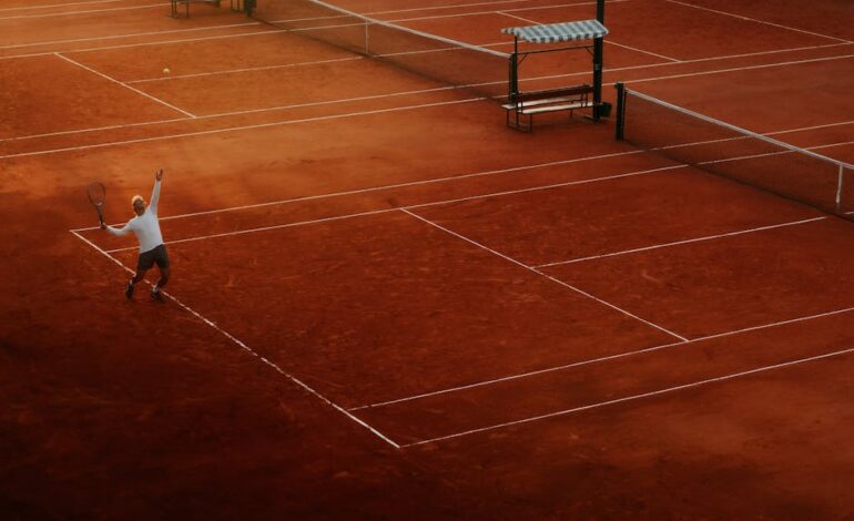 A player serves on a clay tennis court, highlighting the beauty and intensity of the sport at sunset.