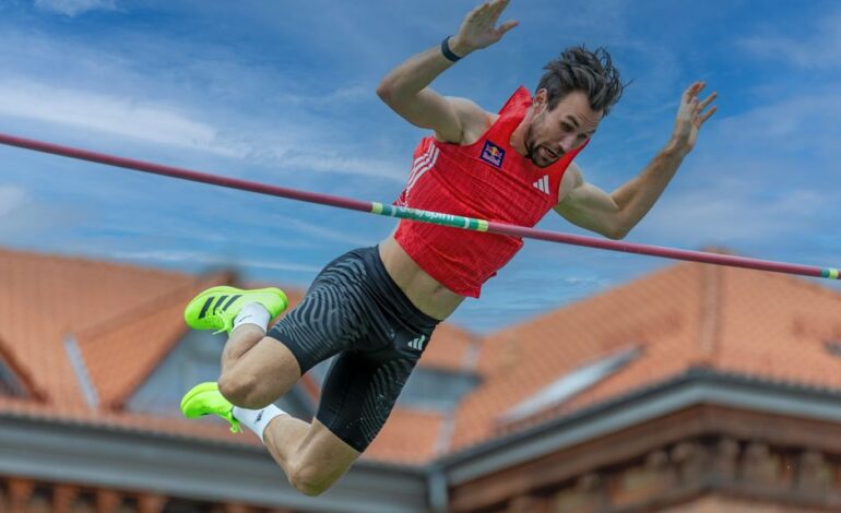 A male athlete captured mid-air during a pole vault attempt against a clear sky.